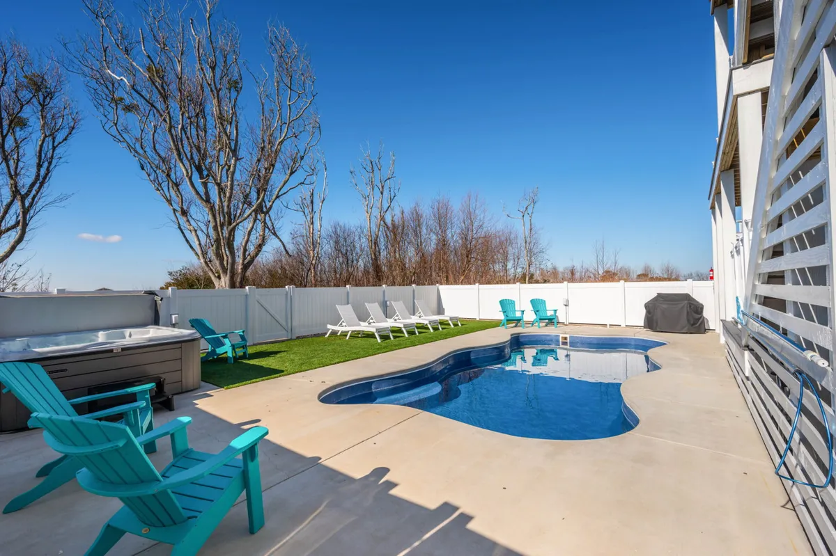 A tranquil backyard scene featuring a sparkling swimming pool, inviting hot tub, lounge chairs, and a fenced yard. The setting is perfect for relaxing, swimming, and socializing in a private outdoor space.