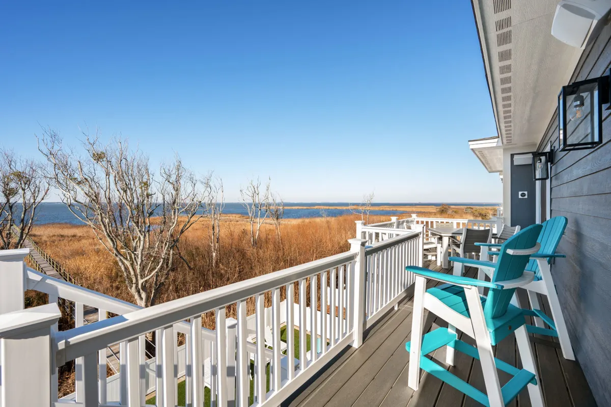 This exterior shot shows a spacious balcony outfitted with comfortable chairs and a stunning view of the water. Dried grasses in the foreground add to the coastal vibe, and the setup is perfect for morning stretches, coffee, or twilight cocktails.