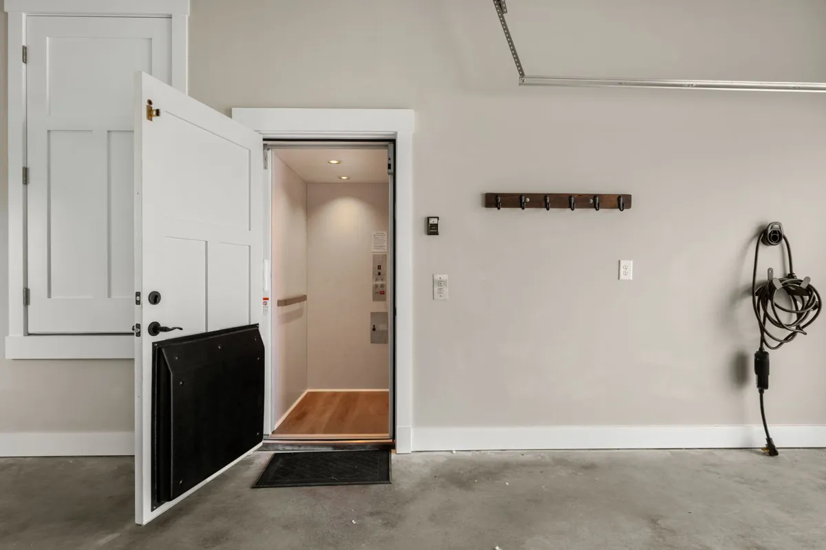 A clear view of the open elevator door inside a pristine garage, with organized wall hooks and a spotless floor. The elevator offers direct access from the garage, emphasizing both convenience and universal accessibility.