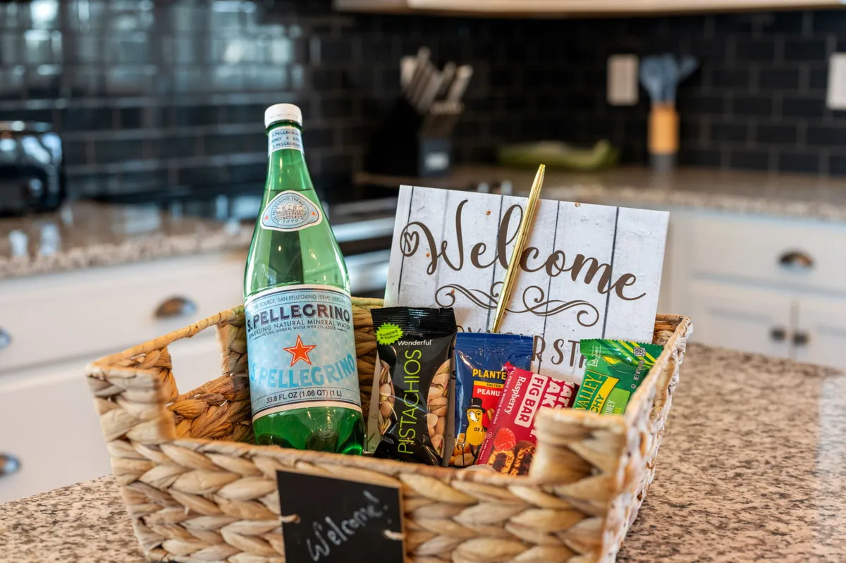 A welcoming kitchen scene featuring a basket with snacks and drinks and a cheerful welcome sign. The ambiance is inviting, suggesting a place where families and groups gather to enjoy snacks, relax, and connect in a central part of the home.