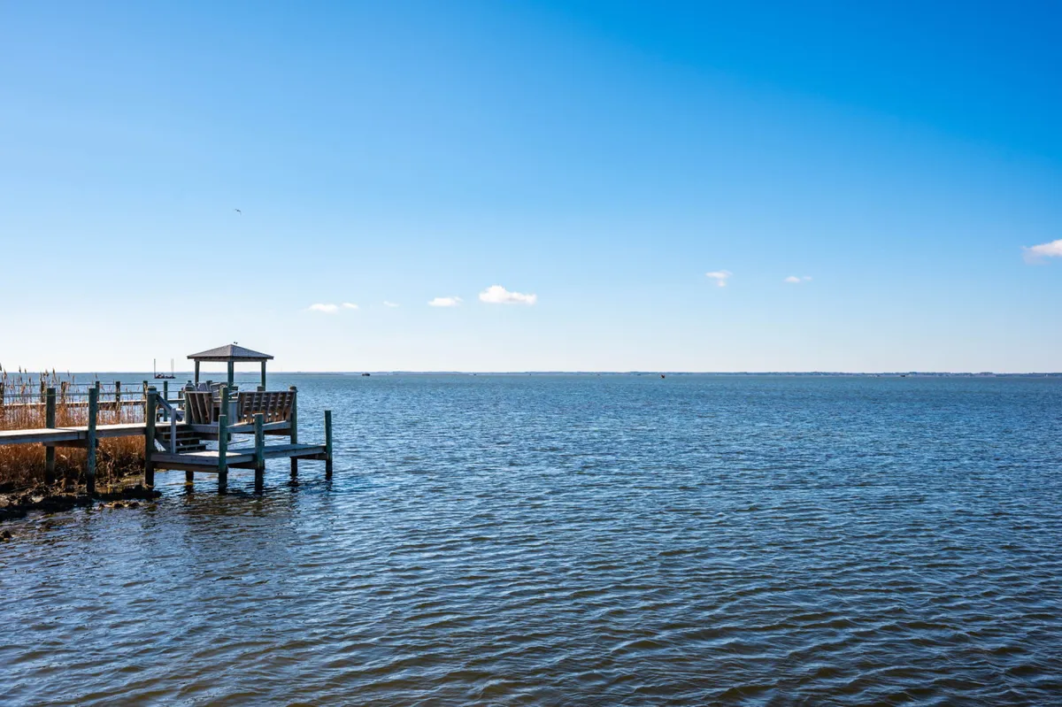A tranquil dock stretches over calm water, with a vast sky overhead. The dock invites peaceful fishing or quiet moments, embodying the serene escape described in the section. The water and open horizon reinforce the neighborhood’s vacation-focused, relaxing vibe.
