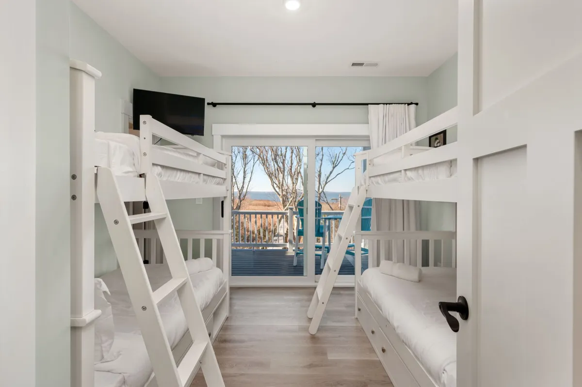 A playful yet cozy bedroom featuring two twin bunk beds, a large window allowing in natural light, and a TV for entertainment. The room is designed with children and families in mind, offering both comfort and a sense of fun.