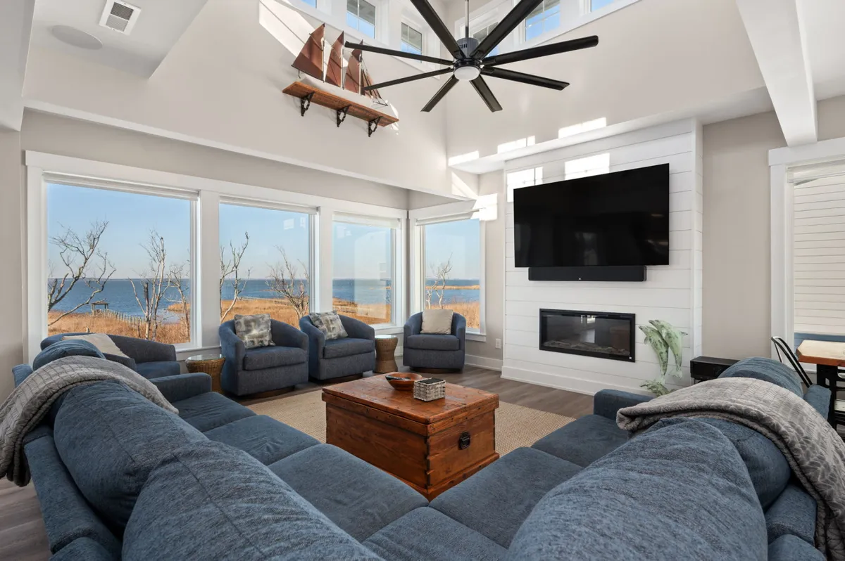 A spacious, inviting living area with comfortable seating, a wooden coffee table, large windows offering water views, and a modern wall-mounted TV. The scene suggests a central family space perfect for enjoying TV entertainment or relaxing together.
