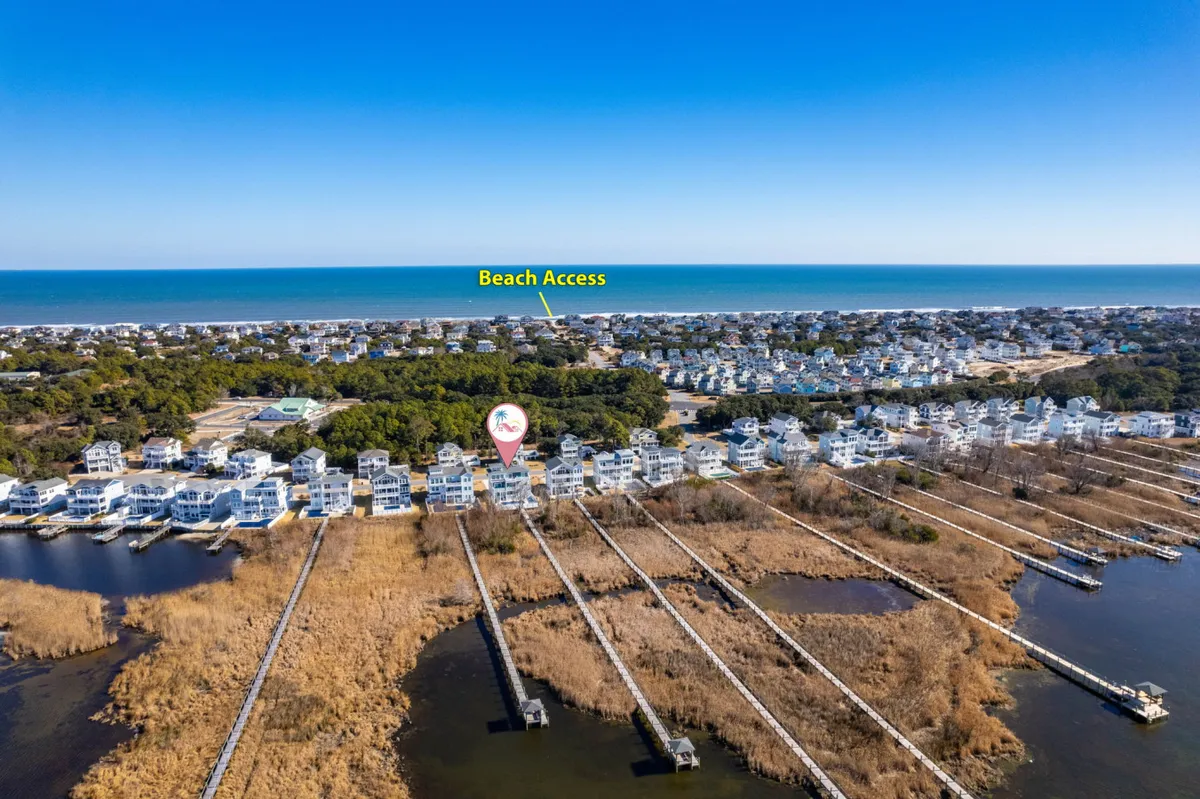 This image shows a scenic beach access point with boardwalks leading through natural landscape towards the ocean, flanked by waterfront homes. The view captures the relaxed and serene mood of Corolla's beachside environment and highlights the proximity and accessibility of the coastline.